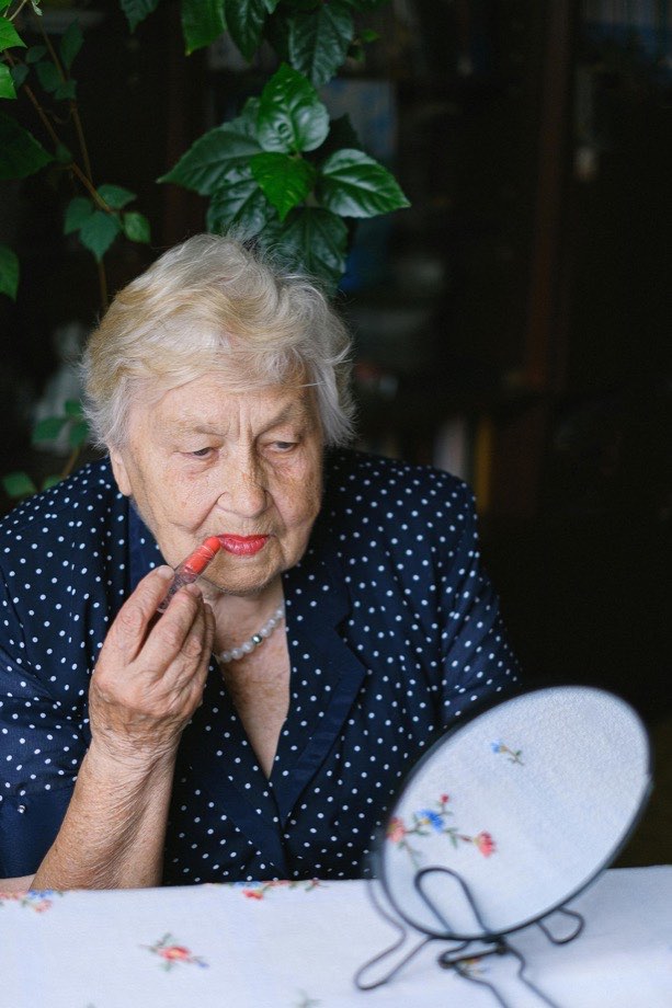 Older woman putting on lipstick at home
